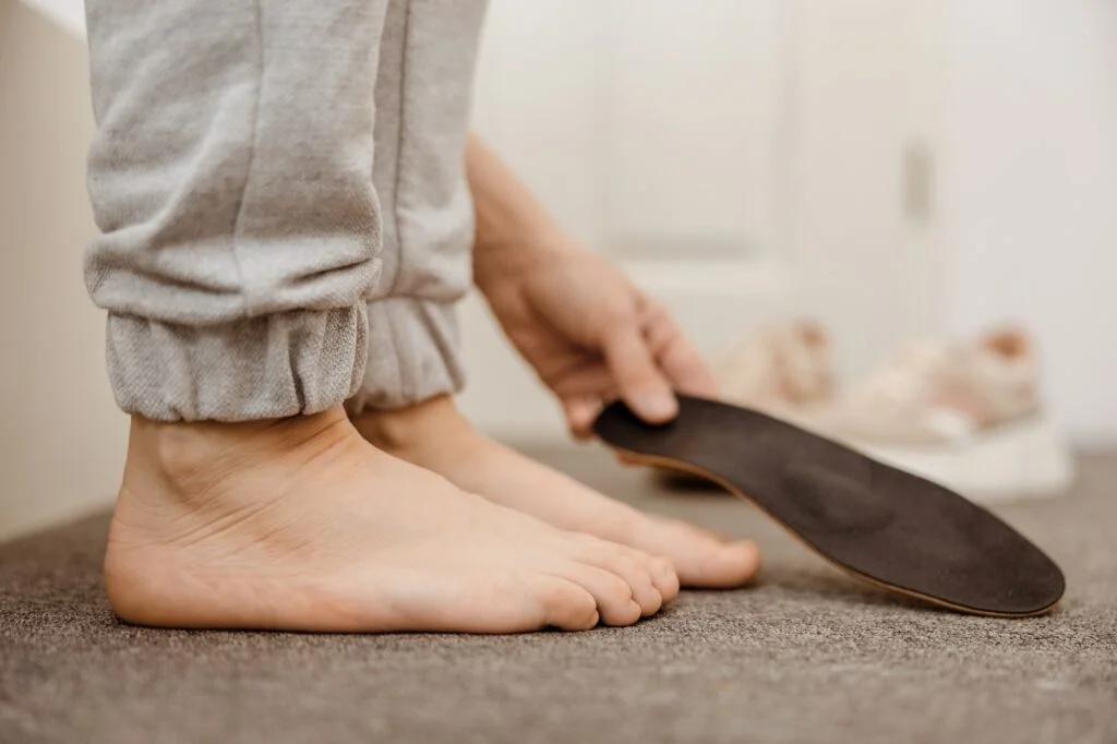 Person holding a custom foot orthotic next to their bare feet.